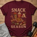 Maroon t-shirt with "SNACK SEASON" text and holiday-themed snack and fitness graphics.
