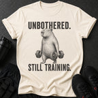 T-shirt with capybara lifting dumbbells and text "UNBOTHERED. STILL TRAINING."
