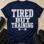 Navy t-shirt with white distressed text reading "TIRED BUT TRAINING" and a barbell graphic.