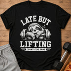 Black t-shirt with graphic of sleepy sloth on a barbell, text "LATE BUT LIFTING COUNTS THE SAME".