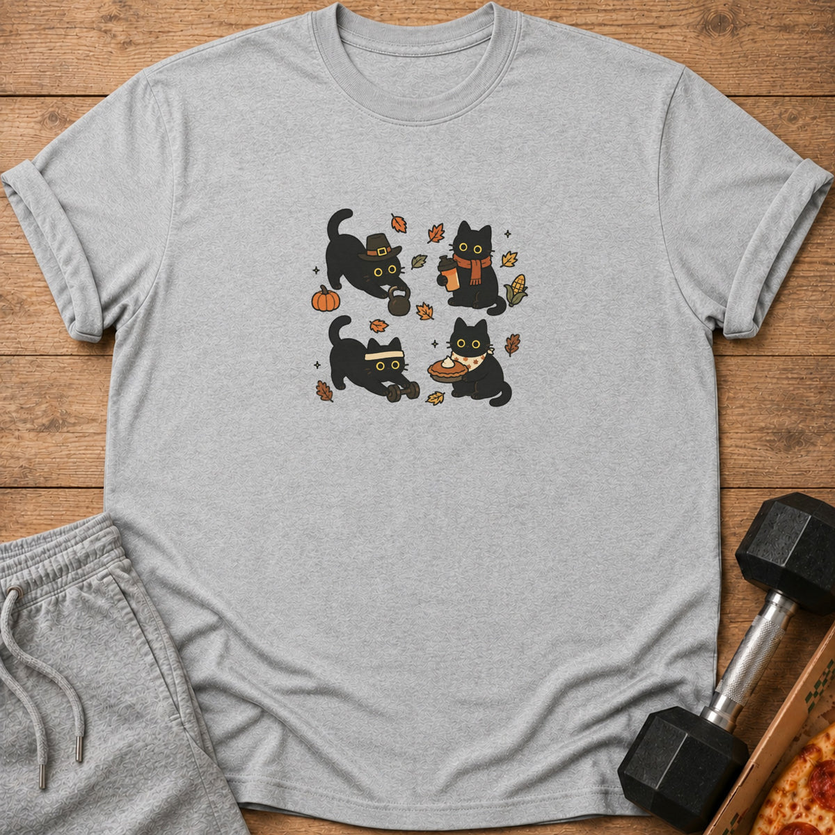 Four cartoon black cats depicted with autumn-themed activities on a gray t-shirt.