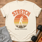 Cream t-shirt with "STRETCH Barely committed" and a figure stretching at sunset.