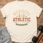 Cream t-shirt with "Mediocre Athletic Club" text and a dumbbell with pizza.