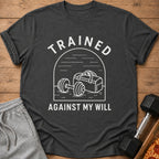 Dark grey t-shirt with "TRAINED AGAINST MY WILL" text and gym bag illustration.
