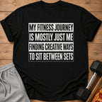 Black t-shirt with "My fitness journey is mostly just me finding creative ways to sit between sets" text.
