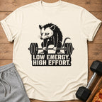 Shirt with a sad possum lifting a barbell and text "LOW ENERGY. HIGH EFFORT."