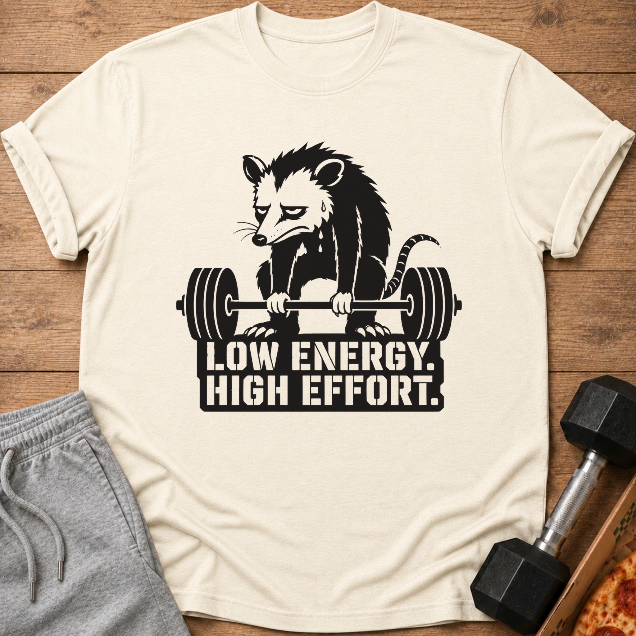 Shirt with a sad possum lifting a barbell and text "LOW ENERGY. HIGH EFFORT."