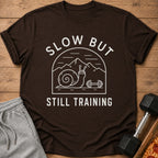 Brown t-shirt with "SLOW BUT STILL TRAINING" text and a snail lifting weights.