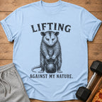 Light blue t-shirt with opossum lifting kettlebell, "LIFTING AGAINST MY NATURE." text.