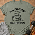 Green t-shirt with text "BUILT DIFFERENT BARELY FUNCTIONING" and cartoon kettlebell.