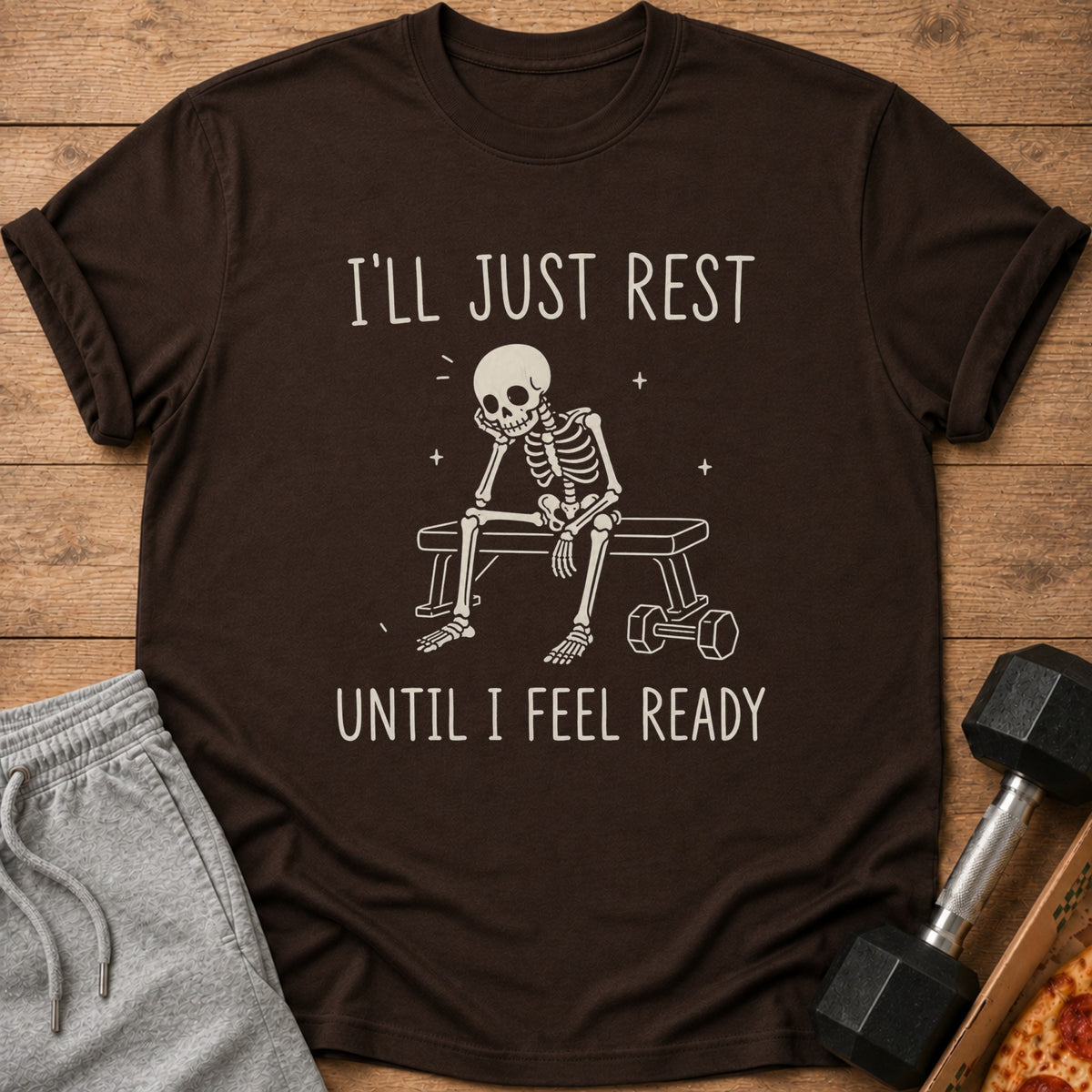 Brown t-shirt with a skeleton sitting on a bench with text: "I'LL JUST REST UNTIL I FEEL READY".