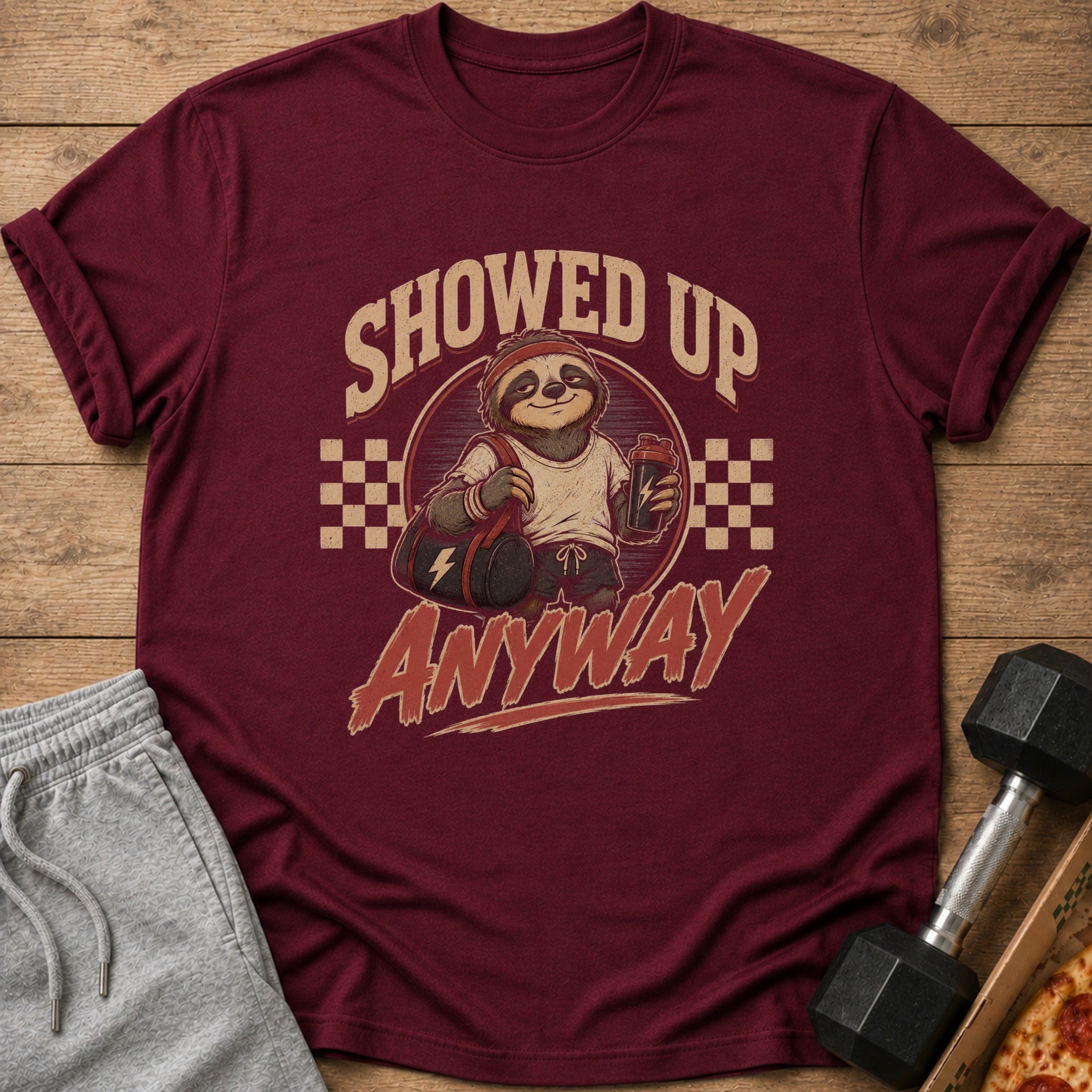 Maroon t-shirt with a sloth wearing a headband holding a gym bag and shaker bottle, text says "SHOWED UP ANYWAY".