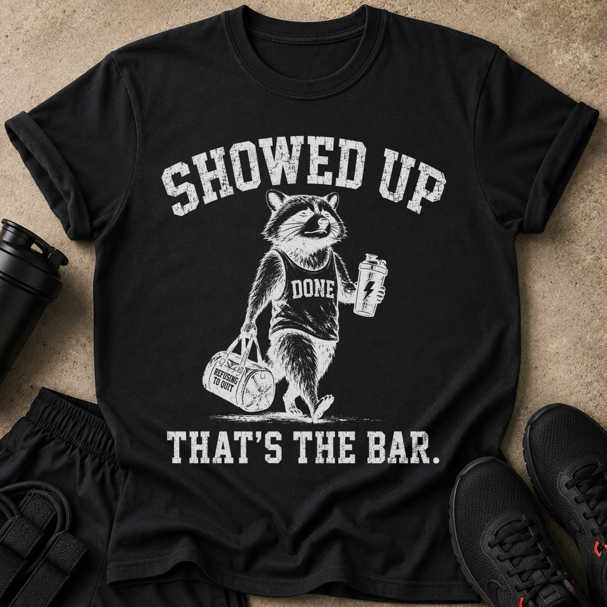 Black t-shirt with raccoon graphic, text "SHOWED UP DONE REFUSING TO QUIT THAT'S THE BAR."