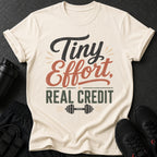 Cream t-shirt with "Tiny Effort, Real Credit" text and a dumbbell graphic.