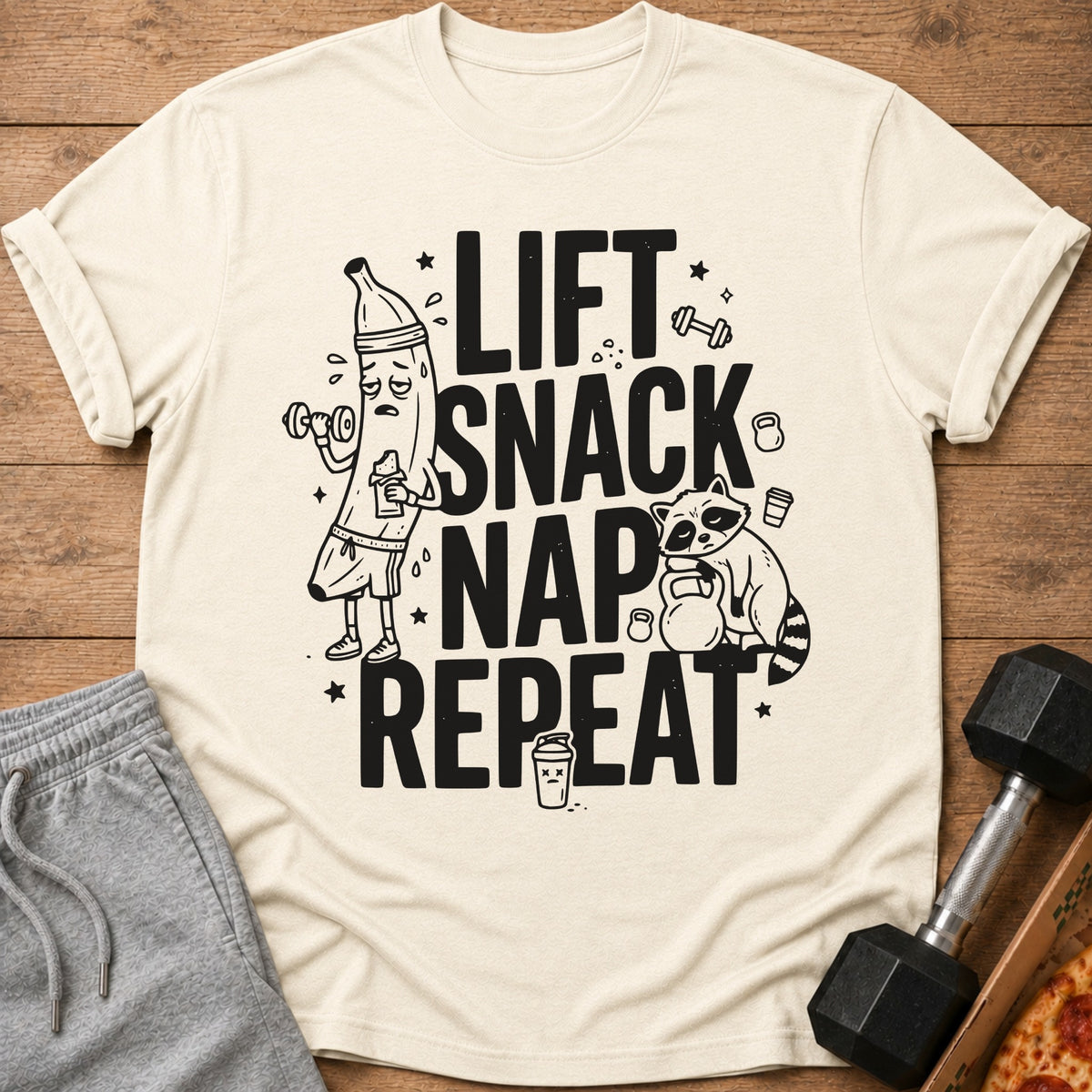 Shirt with "Lift Snack Nap Repeat" text, featuring cartoon banana and raccoon.