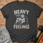 Dark gray t-shirt with distressed graphic of a man hugging a dumbbell, text reads "HEAVY FEELINGS".
