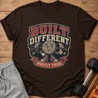 Brown t-shirt with "BUILT DIFFERENT MOSTLY TIRED" graphic featuring a tired dumbbell character.