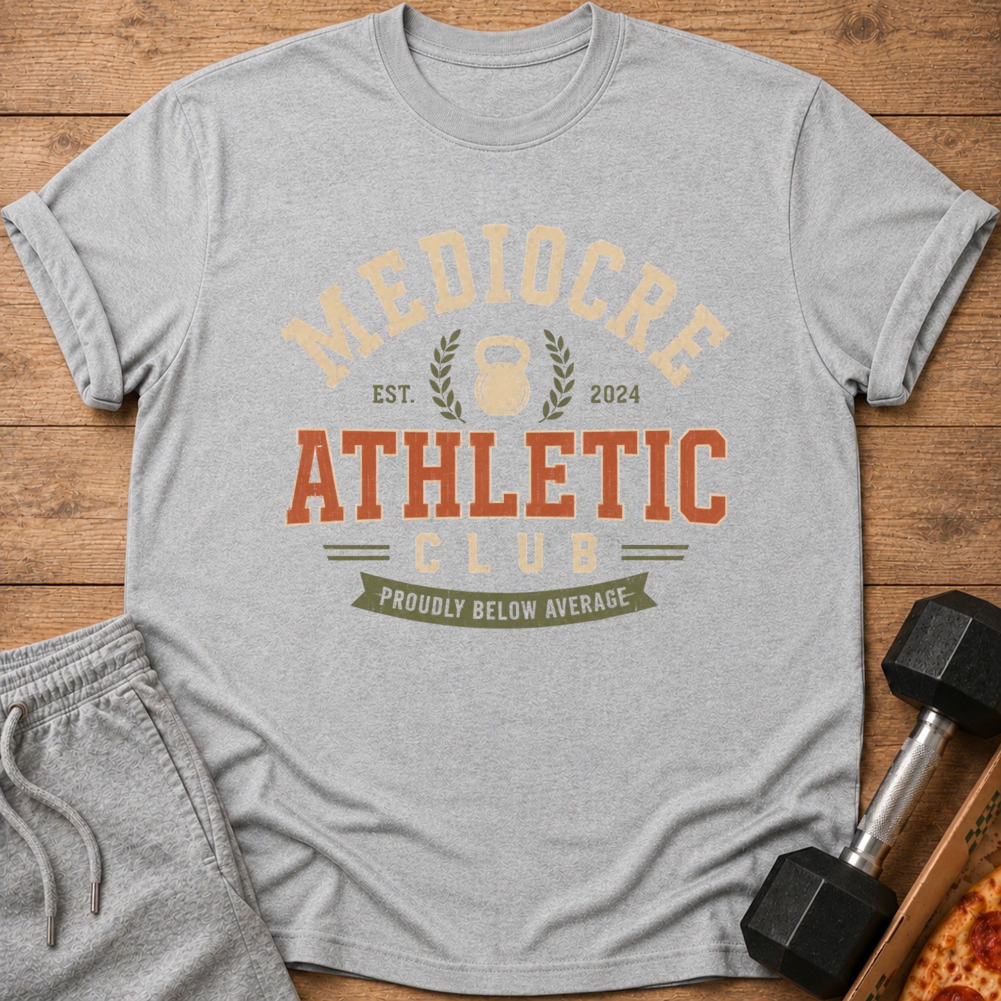 Grey t-shirt with "Mediocre Athletic Club" and "Proudly Below Average" text and kettlebell graphic.