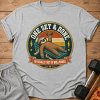 Gray t-shirt graphic of a sloth lying on a bench press, holding a dumbbell.