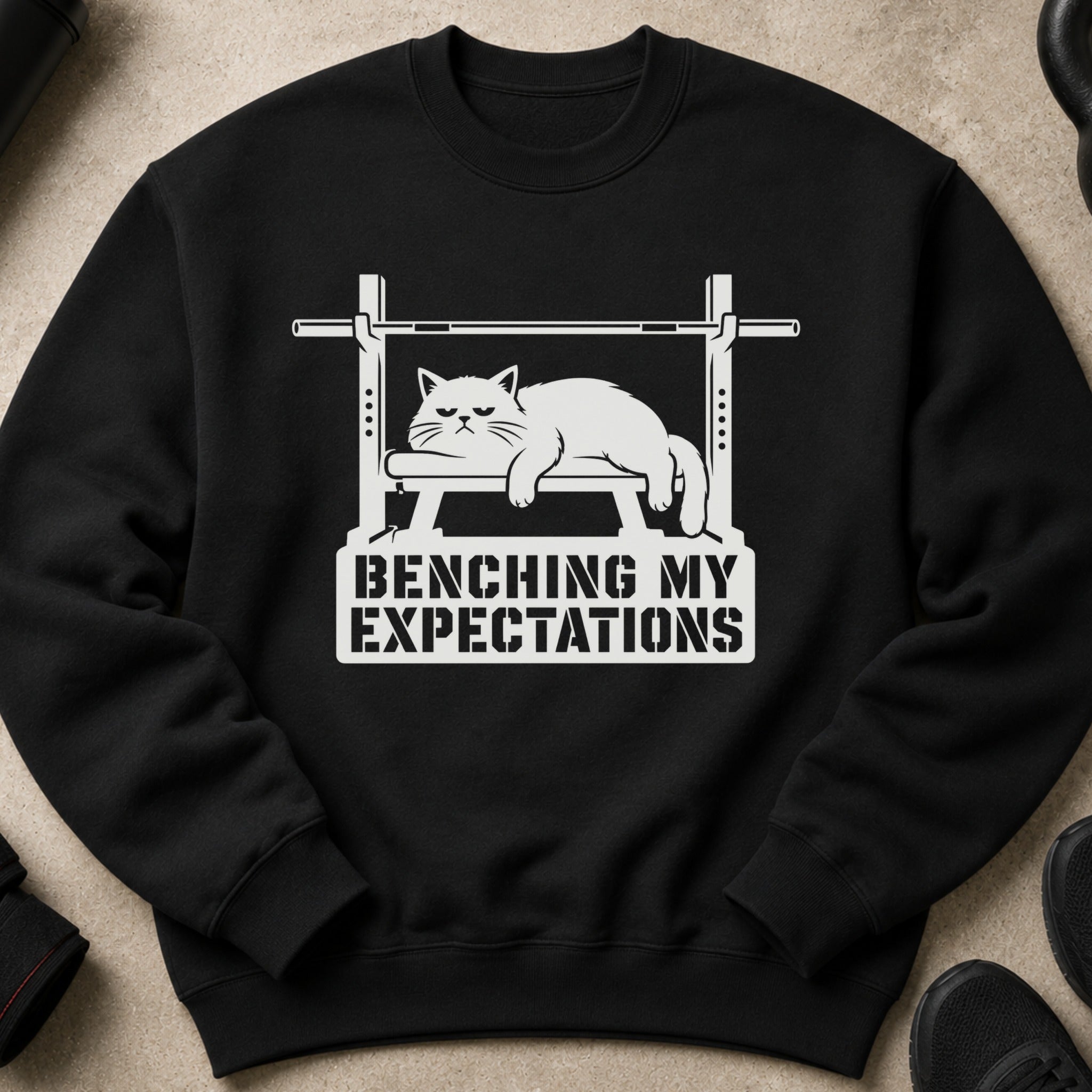 Black sweatshirt with a white graphic of a cat on a bench press, reading "BENCHING MY EXPECTATIONS".
