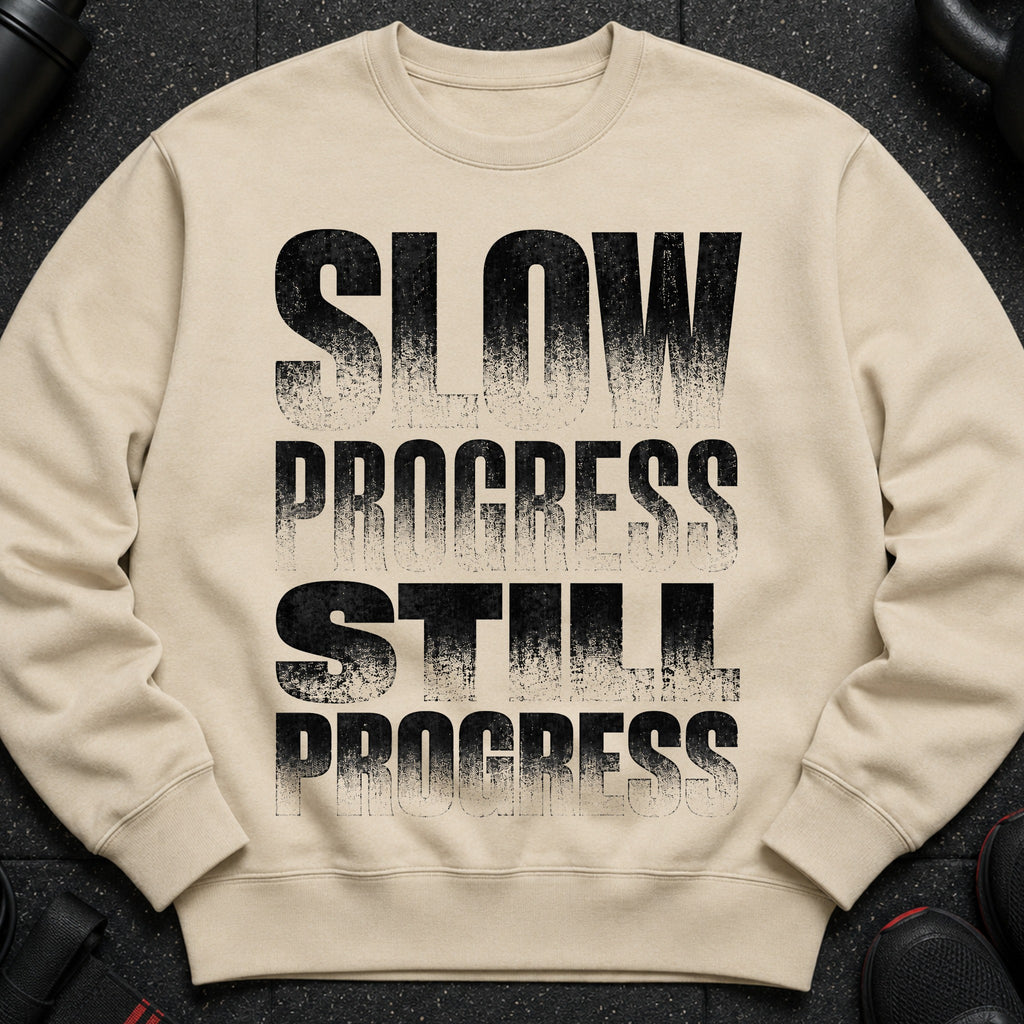 Light beige crewneck sweatshirt with black distressed text "SLOW PROGRESS STILL PROGRESS".