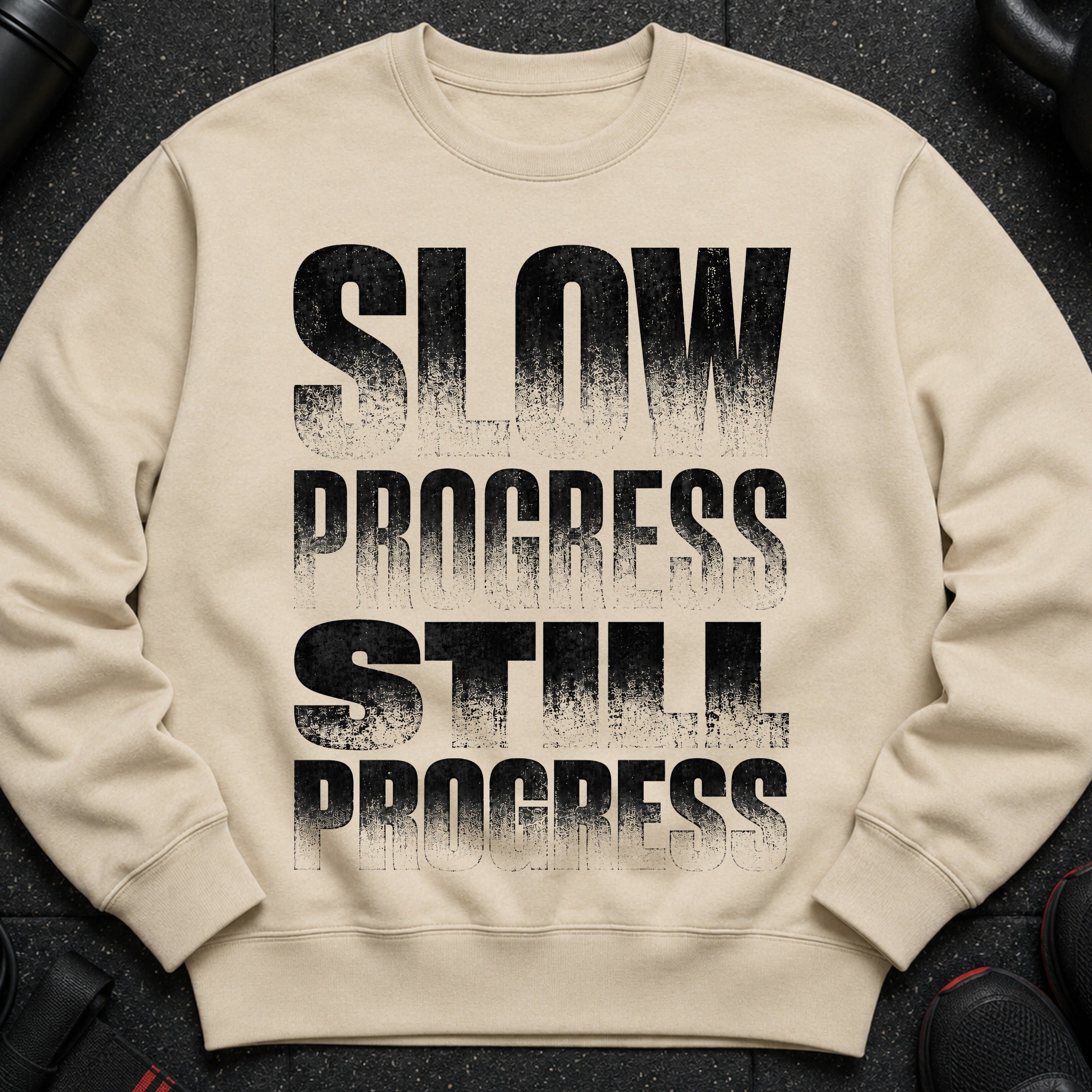Light beige crewneck sweatshirt with black distressed text "SLOW PROGRESS STILL PROGRESS".