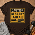 Brown t-shirt with a distressed yellow sign graphic reading "CAUTION REST DAY AHEAD" and a foam roller.