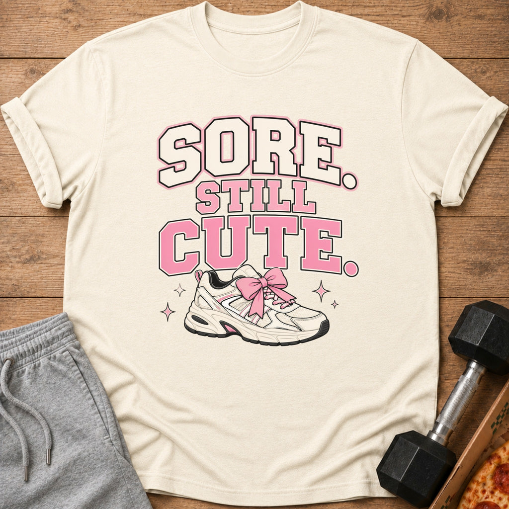 Light cream t-shirt with "Sore Still Cute" and a sneaker with a pink bow.