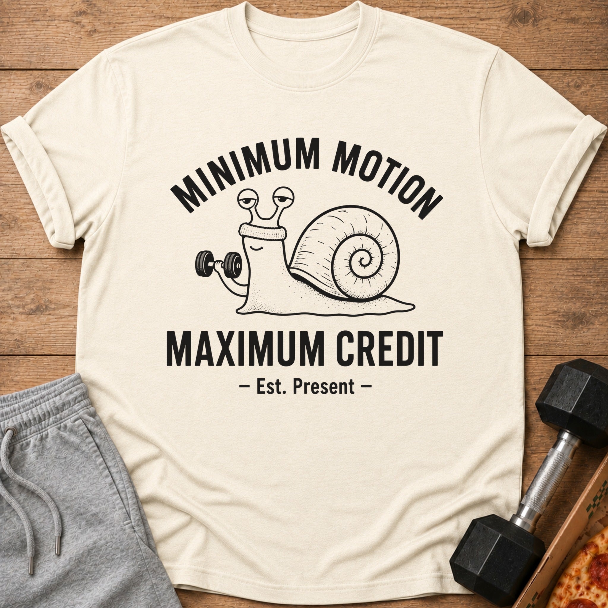 Cream t-shirt with a snail lifting a dumbbell and text "MINIMUM MOTION MAXIMUM CREDIT".