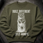 Olive green sweatshirt with a cat holding a kettlebell and text reading "BUILT DIFFERENT", "MOSTLY ANNOYE".