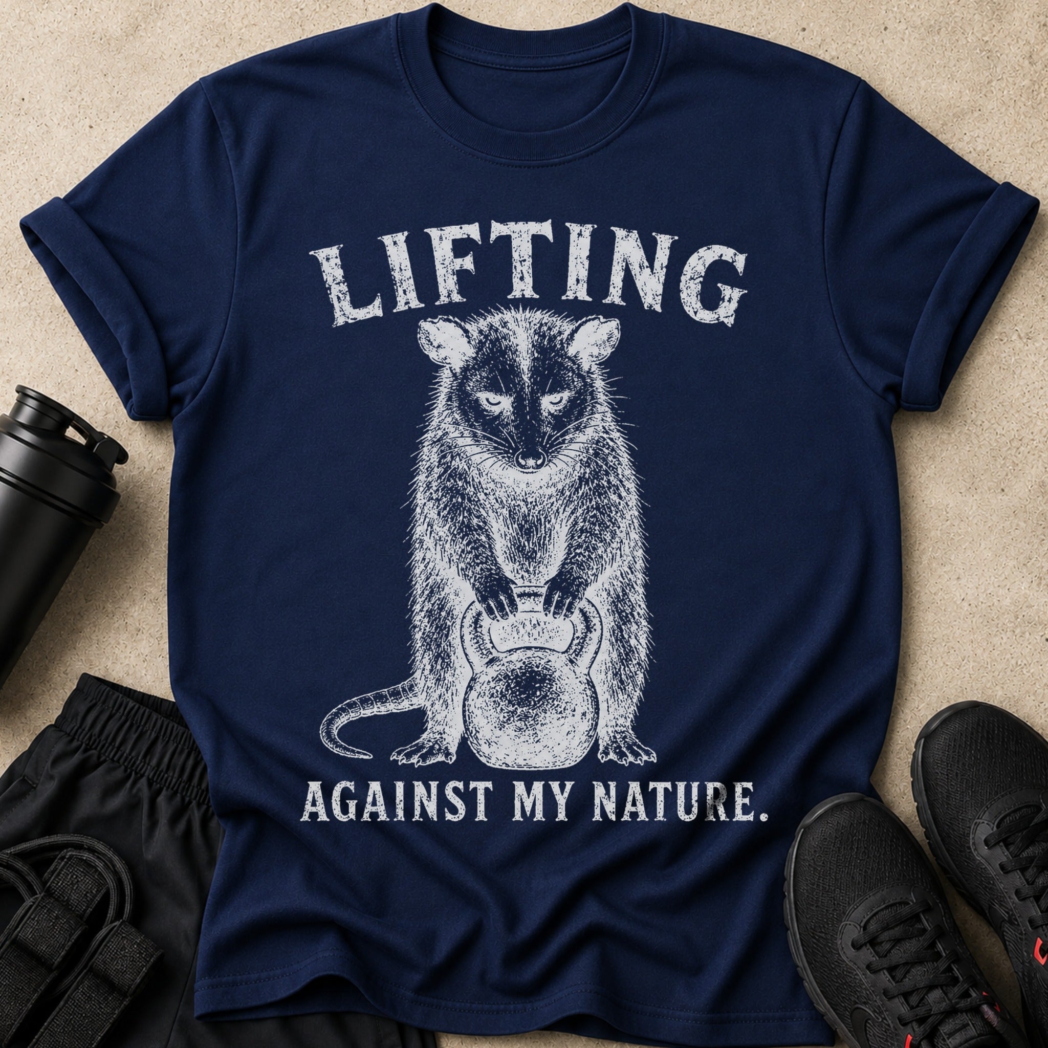 Navy t-shirt with text "LIFTING AGAINST MY NATURE" and a drawing of a possum holding a kettlebell.