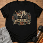 Black t-shirt with a cat wearing a headband lying on dumbbells, text reads "SORE BUT FINE."