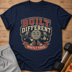 Navy t-shirt with cartoon weightlifting barbell character and text "BUILT DIFFERENT MOSTLY TIRED."