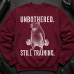 Maroon sweatshirt with a white graphic of a capybara holding dumbbells and text "UNBOTHERED. STILL TRAINING."