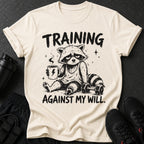 T-shirt with a tired raccoon holding coffee, lifting weights, and text "TRAINING AGAINST MY WILL."