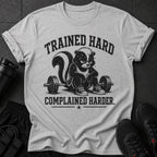 Grey t-shirt with a cartoon skunk sitting on a barbell, text reads "Trained Hard Complained Harder."