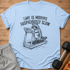 Light blue t-shirt with raccoon on treadmill graphic and text "TIME IS MOVING SUSPICIOUSLY SLOW".