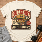 T-shirt graphic with a cartoon burger lifting weights and text "Bulking? Just Hungry."