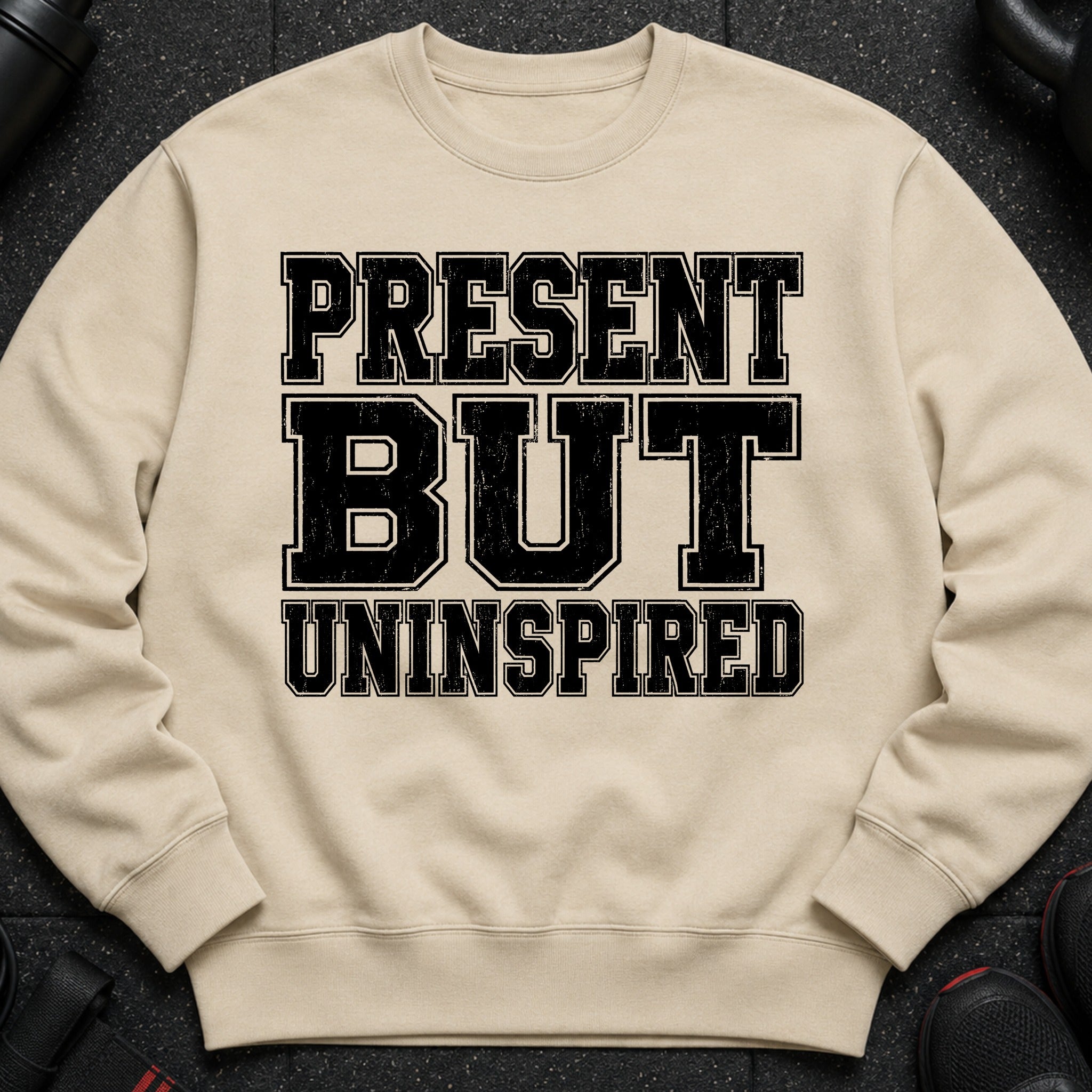 Light beige sweatshirt with distressed black text "PRESENT BUT UNINSPIRED".