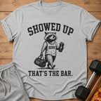 Graphic t-shirt with raccoon wearing "DONE" tank top, carrying gym bag and shaker.