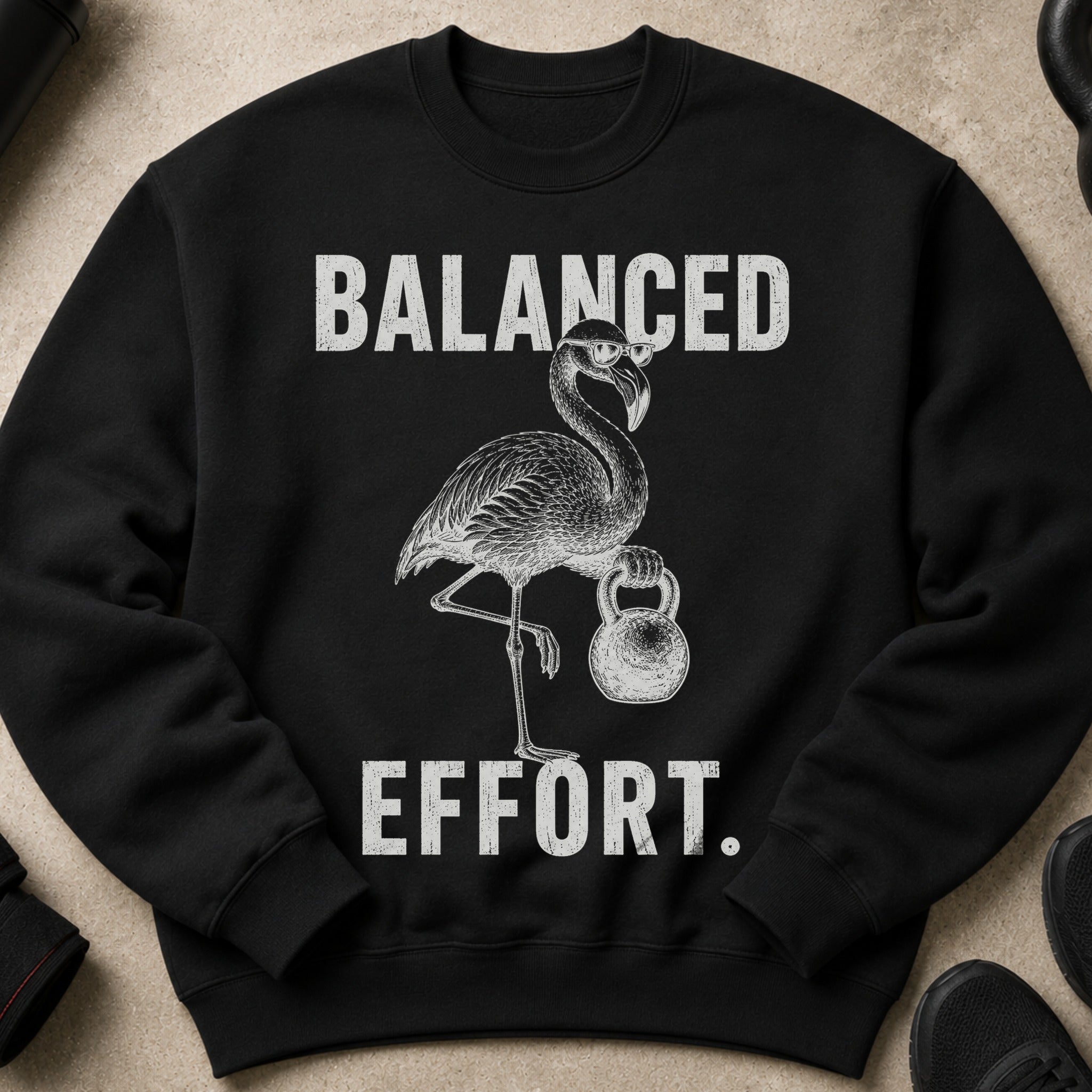 Black sweatshirt with distressed text "BALANCED" above a flamingo holding a kettlebell and "EFFORT."
