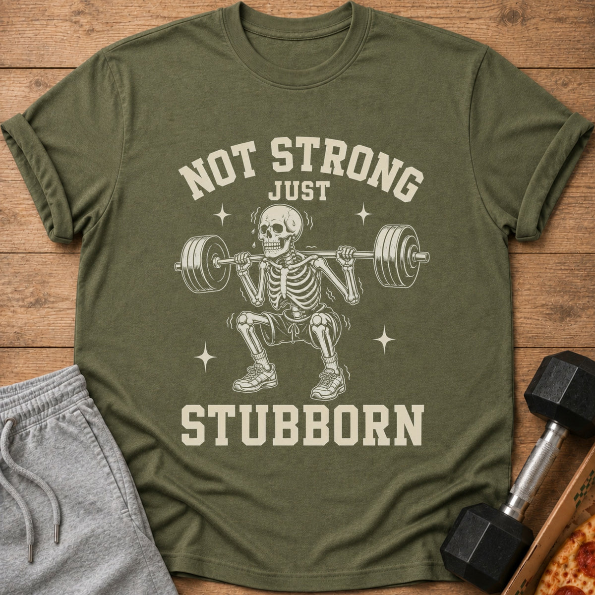 T-shirt with skeleton lifting weights and text "NOT STRONG JUST STUBBORN".