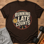 Brown t-shirt with distressed circular graphic of a stopwatch and road, saying "RUNNING LATE COUNTS".