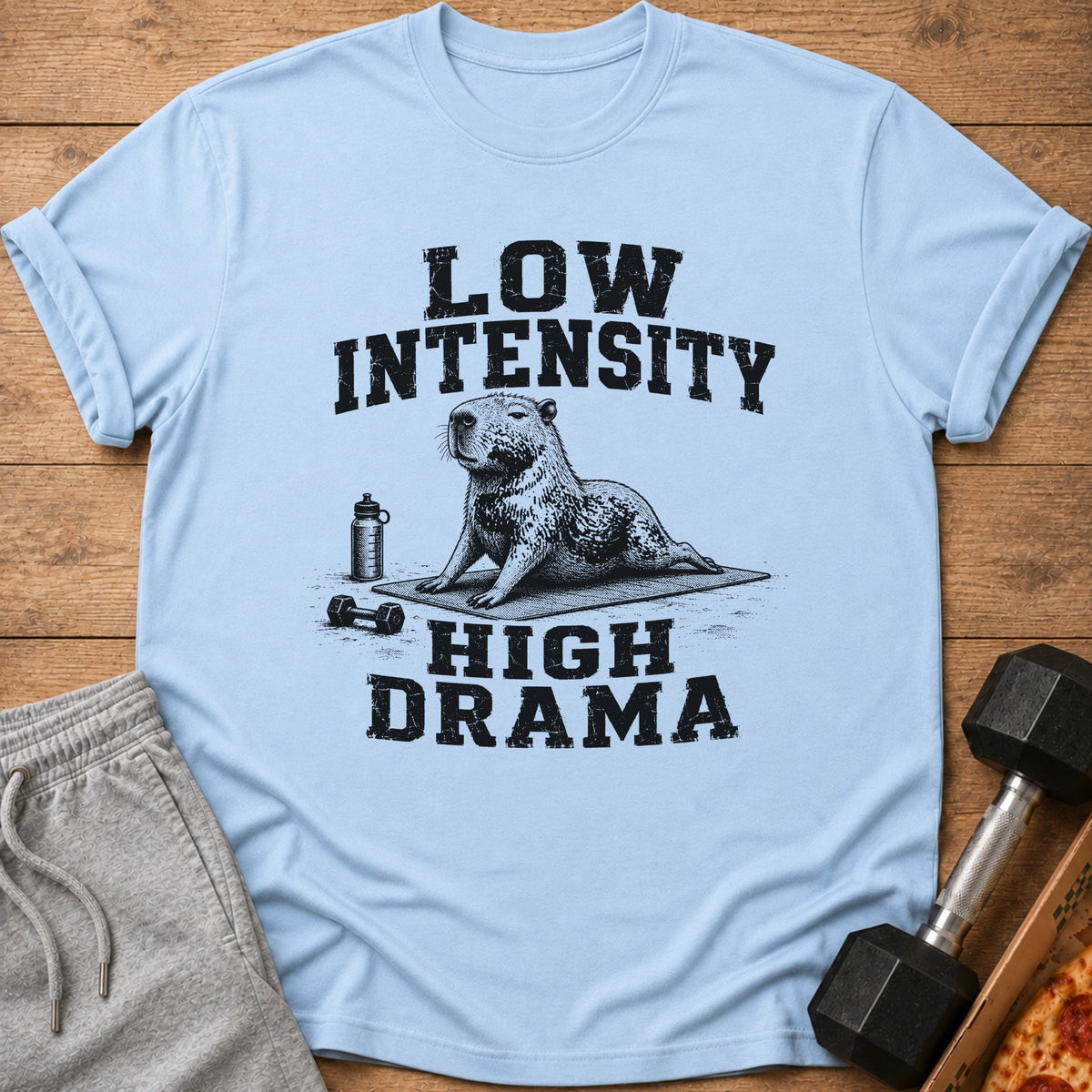 Light blue t-shirt with a capybara doing yoga and the text "Low Intensity High Drama".
