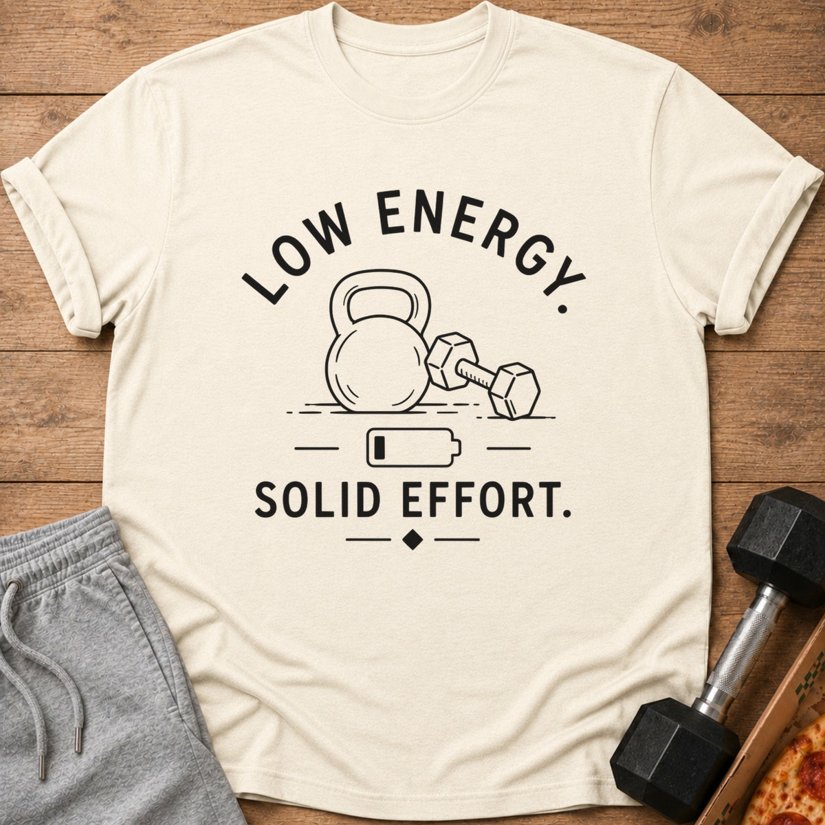 Cream t-shirt with "LOW ENERGY. SOLID EFFORT." text, kettlebell, dumbbell, and battery icon.