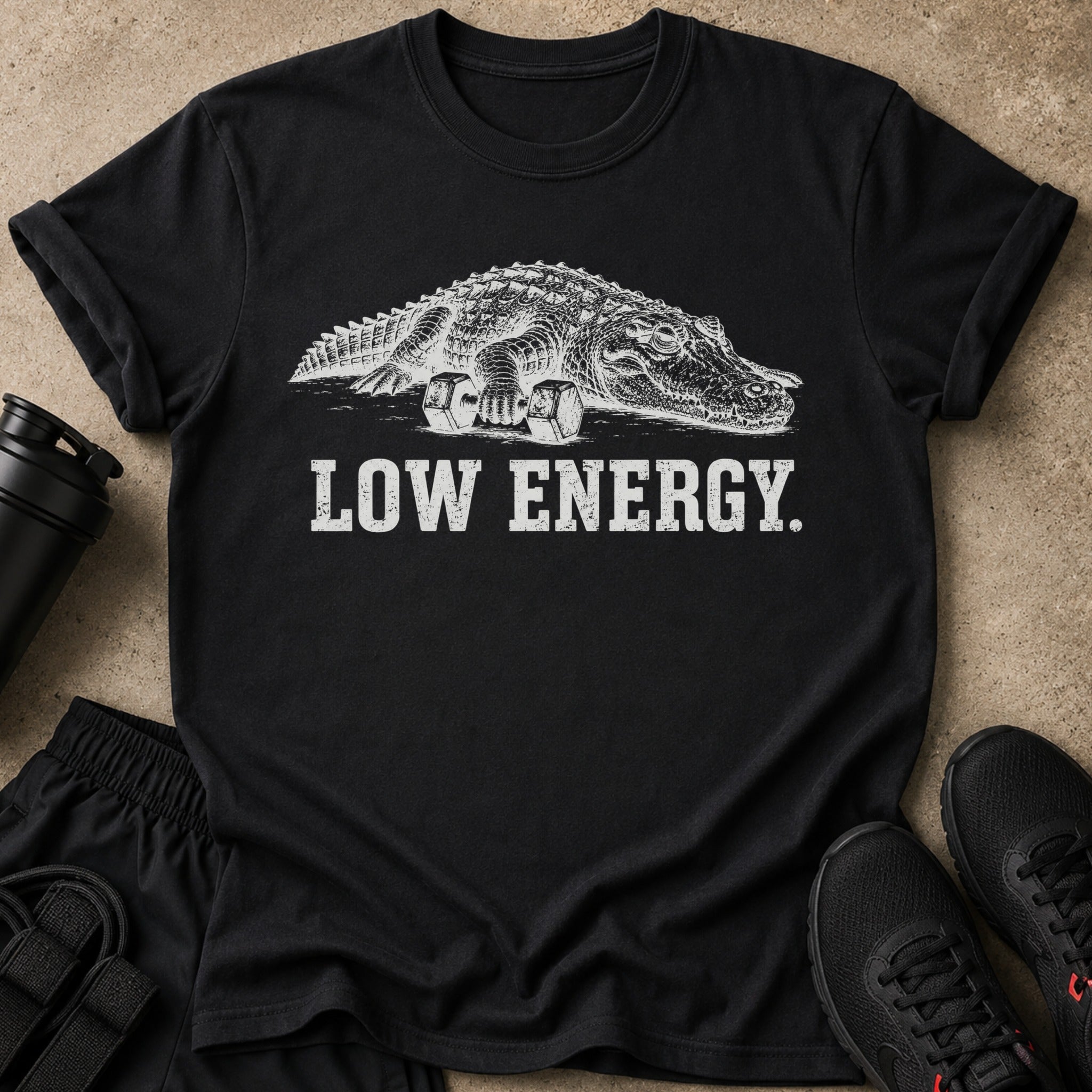 Black t-shirt featuring a white illustration of an alligator on dumbbells with text "LOW ENERGY."
