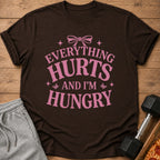 Brown t-shirt with pink text that says "Everything Hurts And I'm Hungry".
