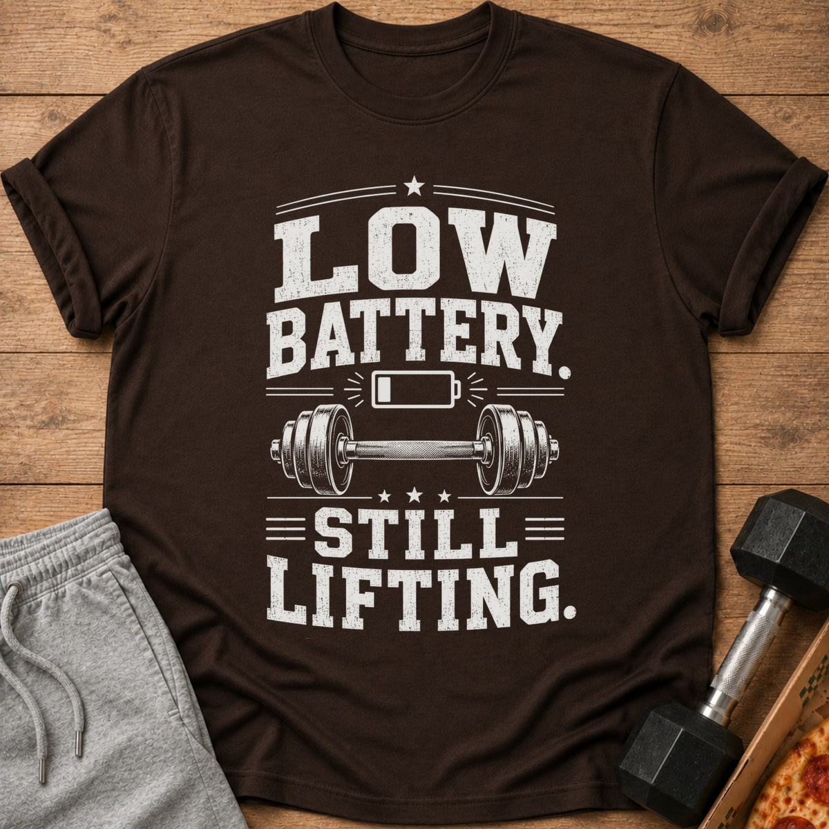 Brown t-shirt with "LOW BATTERY. STILL LIFTING." text and barbell graphic.