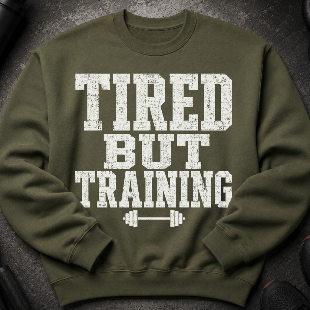 Olive green sweatshirt with distressed white text reading "TIRED BUT TRAINING" and a barbell icon.