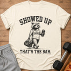 Raccoon wearing "DONE" shirt holding gym bag and shaker with text "SHOWED UP THAT'S THE BAR."